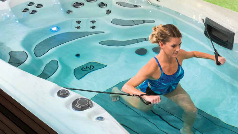 Meilleurs spas de nage : une femme en maillot de bain bleu effectue un exercice d'aviron dans un spa de nage H2X Fitness