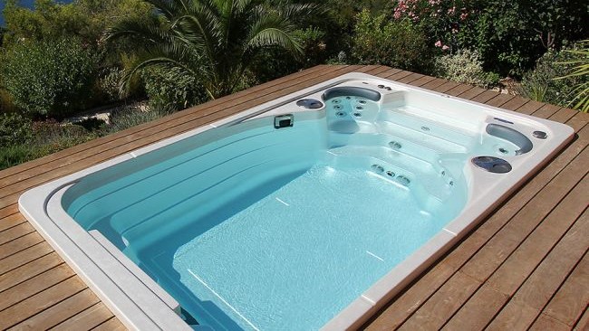 Meilleurs spas de nage : un Hydropool est installé dans une terrasse de couleur teck dans un jardin verdoyant